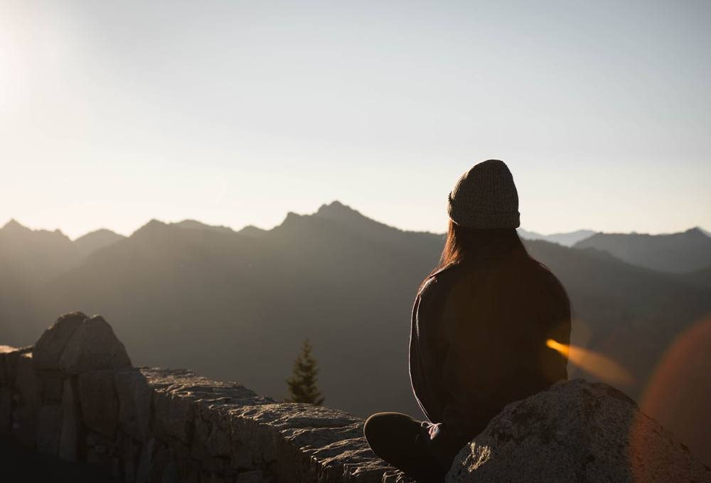 Femme assise face aux montagnes au lever du soleil, posture calme et assurée
