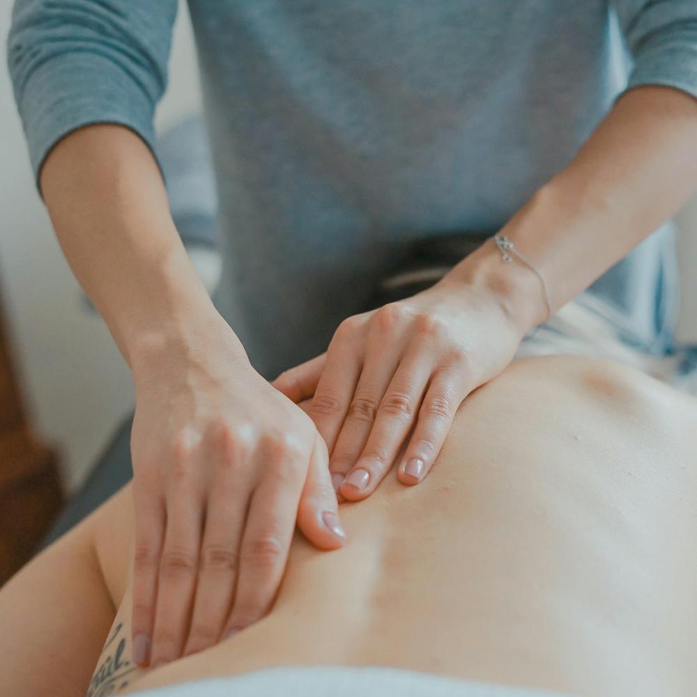 Mains posées sur le dos d'une personne allongée sur une table de soin